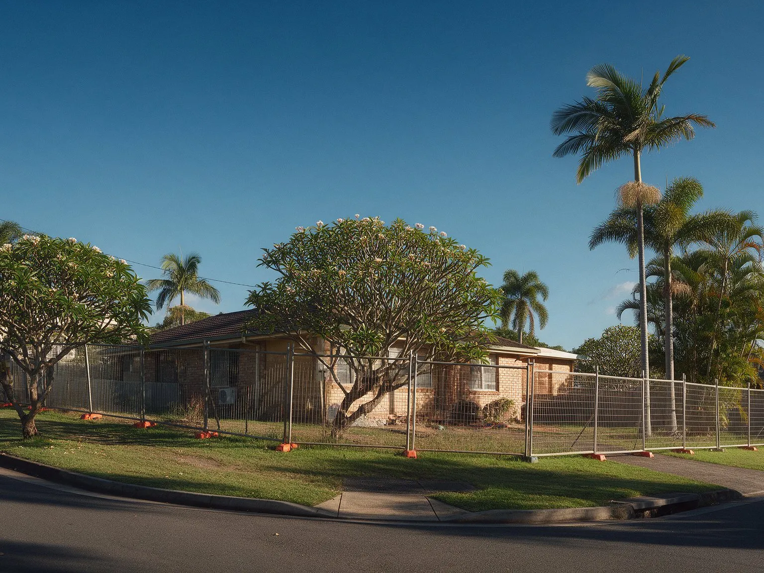 Representative image: an older low-set brick house on a wide corner block with temporary fencing in a Brisbane suburb