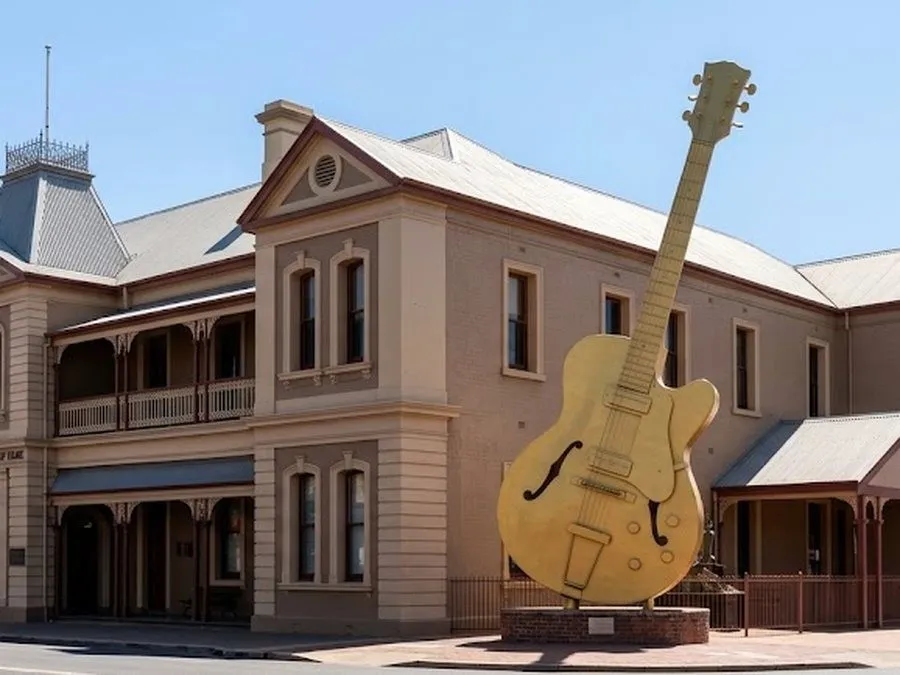 A two-storey heritage hotel on a country-town main street with a giant golden guitar beside it